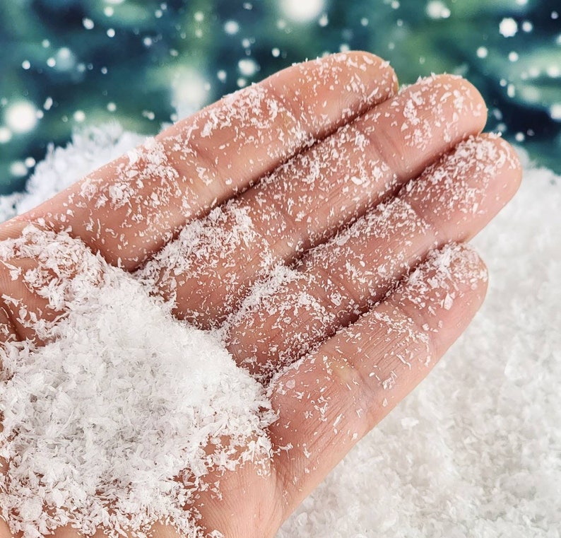 May include: A hand covered in white, fluffy fake snow. The snow is loose and resembles a light, powdery snow.