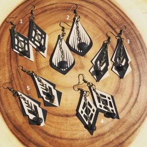 Puede incluir: Cinco pares de pendientes de cuero blanco y negro con detalles de roca volcánica negra. Cada par es único y presenta un patrón geométrico diferente.