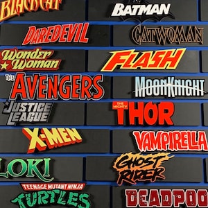 May include: A wall display of colorful comic book character logos, including Batman, Hulk, Thor, Daredevil, and Wonder Woman.