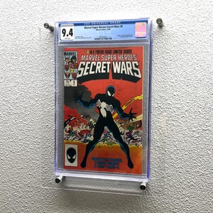 May include: A graded comic book, Marvel Super Heroes Secret Wars #8, encased in a clear protective holder. The cover features a black and white Spider-Man figure against a red and orange background. The grade is 9.4.