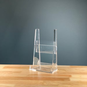 May include: A clear acrylic book stand with two shelves. The stand is designed to hold books or other items upright.