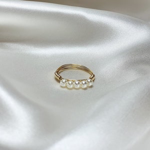 May include: A gold wire ring with five white pearls.