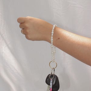 May include: A white pearl keychain with a silver key ring and a black car key with a pink and white beaded charm that says "DRIVE SAFE".
