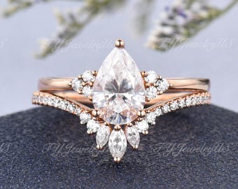 Puede incluir: Un juego de anillos de compromiso de oro rosa con una piedra central de diamante en forma de pera y una banda a juego. El anillo principal presenta un halo de diamantes más pequeños y piedras en forma de marquesa, con el texto "TY JewelryUs".