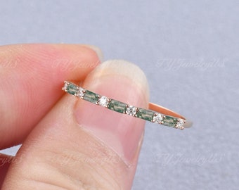 May include: A delicate gold band ring with a row of small, emerald green and clear round gemstones. The ring is set in a simple, minimalist style.