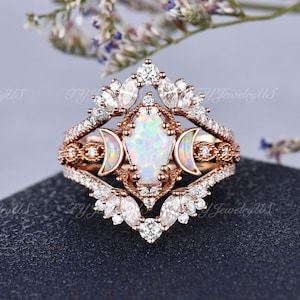 May include: Rose gold ring set featuring an opal center stone, accented with diamonds and moon details. The set includes a main ring and two additional bands, all with intricate designs. The rings are set against a dark background.