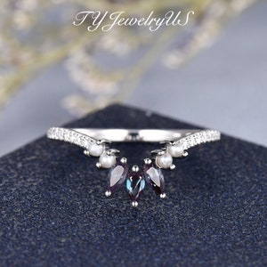 May include: A silver ring with a V-shaped band adorned with small white pearls and cubic zirconia stones. Three marquise-shaped gemstones hang from the center of the band.