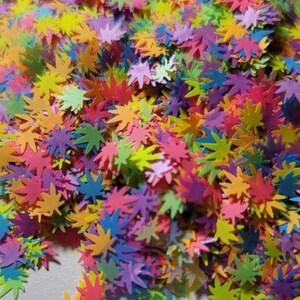 May include: A pile of colorful confetti shaped like cannabis leaves. The confetti is in shades of pink, purple, green, yellow, and orange.