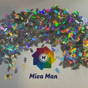 May include: A pile of iridescent holographic glitter in the shape of seahorses. The glitter is scattered on a white surface with a logo in the lower center that reads "Mica Man".