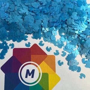 May include: A pile of light blue glitter shaped like ducks. The glitter is on a white surface with a rainbow logo with the letter "M" in the center.