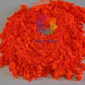 May include: A close-up of a pile of bright orange pigment powder. The powder is fine and has a slightly grainy texture.