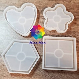 May include: Four silicone moulds for resin casting. The moulds are shaped like a heart, a flower, a hexagon, and a square. Each mould has multiple sections for creating intricate designs.