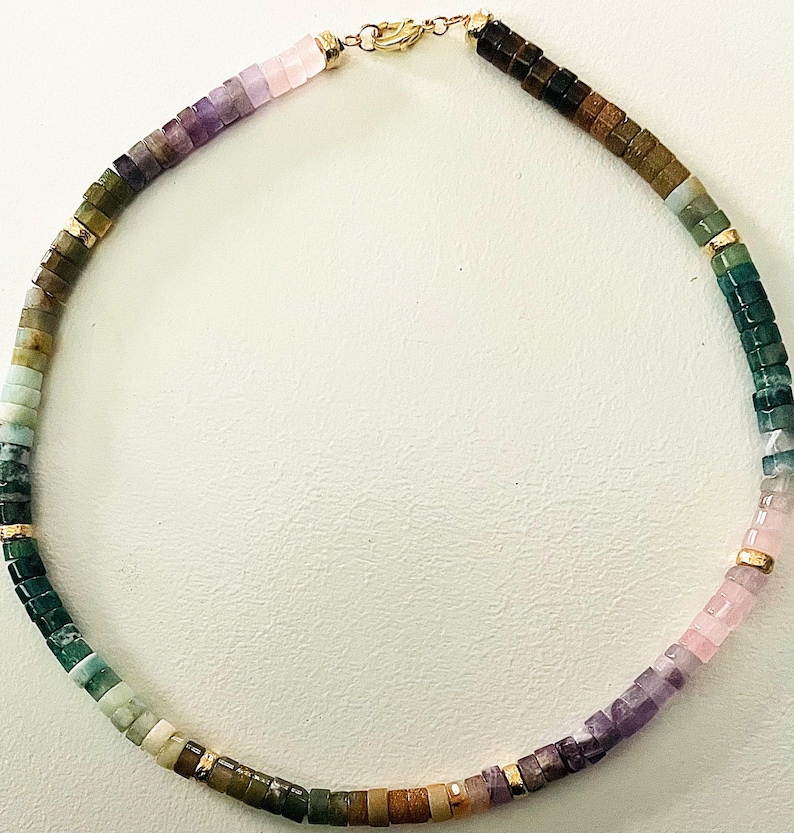 May include: A multi-colored gemstone necklace with a gold clasp. The necklace features a gradient of colors, starting with pink and purple, transitioning to green and brown.
