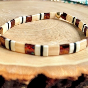 Op de afbeelding: Een beige, bruin, zwart en wit betegeld armband met een gouden sluiting.