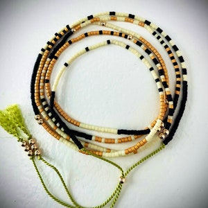 May include: A multi-strand beaded necklace with black, white, and gold beads. The necklace has a green tassel on each end.