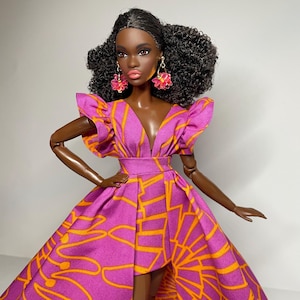 May include: A fashion doll with dark brown skin wearing a pink and orange dress with a high low hemline. The doll has curly black hair and is wearing pink flower earrings.