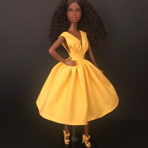 May include: A black doll wearing a yellow sleeveless dress with a V-neckline. The doll has curly black hair and is wearing yellow heels.
