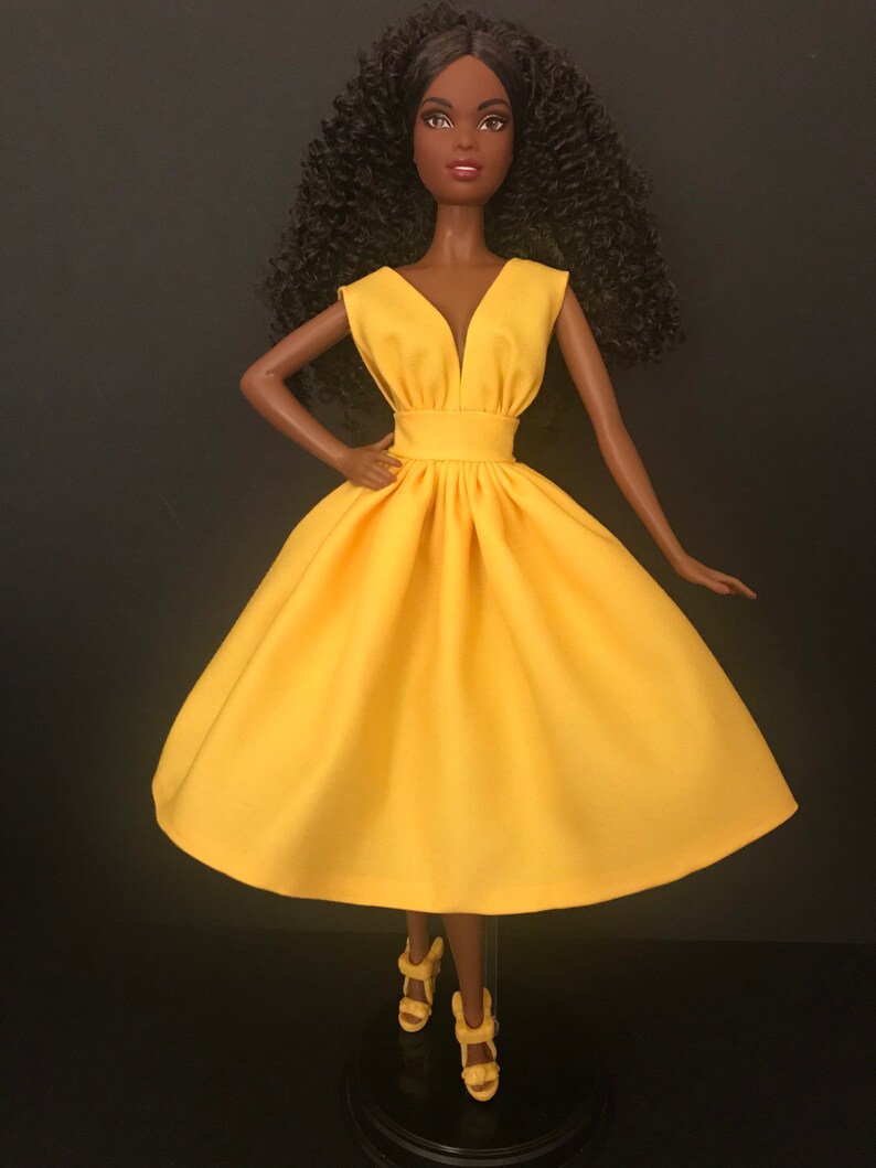 May include: A black doll wearing a bright yellow sleeveless dress with a V-neckline. The doll has curly black hair and is wearing yellow heels.