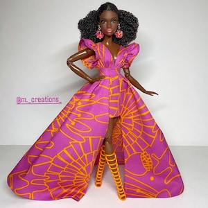May include: A Black doll wearing a pink and orange dress with a high-low hemline. The dress has a V-neckline and ruffled sleeves. The doll is wearing orange high-heeled sandals and has curly black hair. The doll is wearing pink earrings.