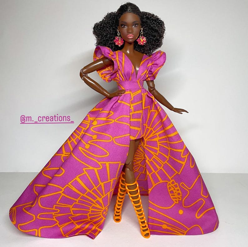 May include: A Black doll wearing a pink and orange dress with a high-low hemline. The dress has a V-neckline and ruffled sleeves. The doll is wearing orange high-heeled sandals and has curly black hair. The doll is wearing pink earrings.