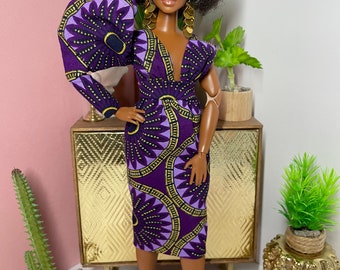 May include: A fashion doll with brown skin and an afro hairstyle wearing a purple and gold patterned dress with a large puff sleeve. The doll is wearing gold earrings and purple shoes.