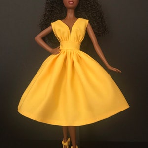 May include: A black doll wearing a bright yellow sleeveless dress with a V-neckline. The dress has a fitted bodice and a full skirt.