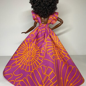 May include: A doll wearing a purple and orange dress with a floral pattern. The dress has a fitted bodice and a full skirt. The doll has dark curly hair.