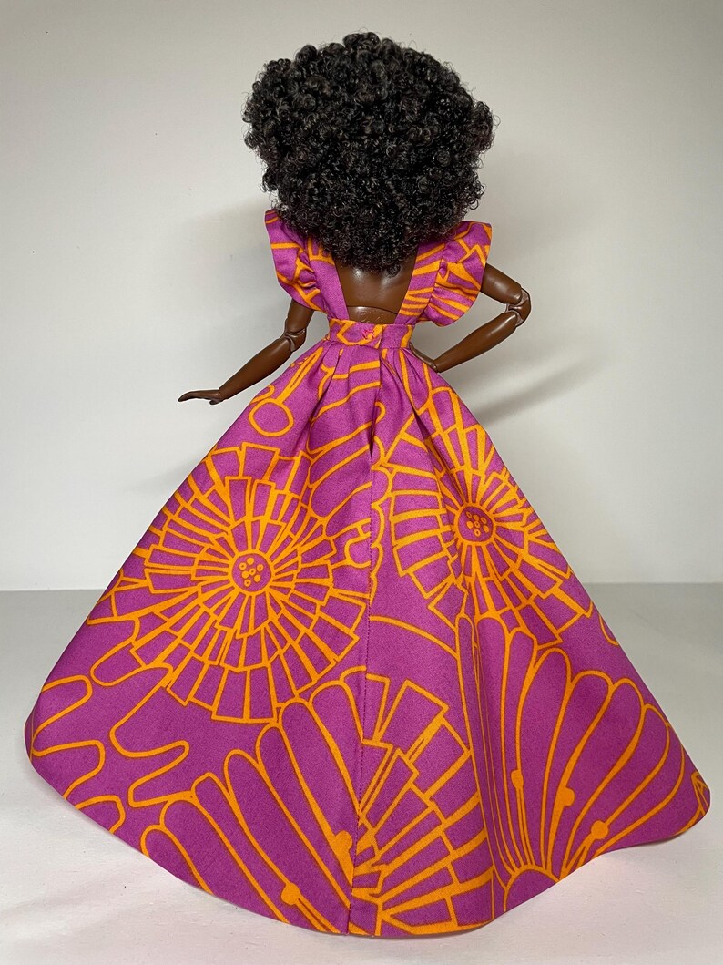 May include: A doll wearing a purple and orange dress with a floral pattern. The dress has a fitted bodice and a full skirt. The doll has dark curly hair.