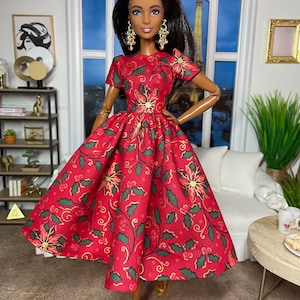Pode incluir: Uma boneca vestindo um vestido vermelho com um padrão floral verde e dourado. O vestido tem uma saia cheia e mangas curtas. A boneca tem cabelo longo e preto e olhos castanhos. Ela está usando brincos dourados e sapatos dourados.