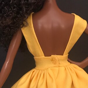 May include: A yellow sleeveless dress with a low back and a button closure. The dress has a gathered skirt and a fitted bodice.