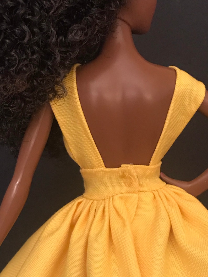 May include: A yellow sleeveless dress with a low back and a button closure. The dress has a gathered skirt and a fitted bodice.