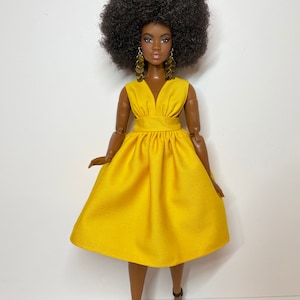 May include: A black doll with an afro hairstyle wearing a yellow dress and black heels.