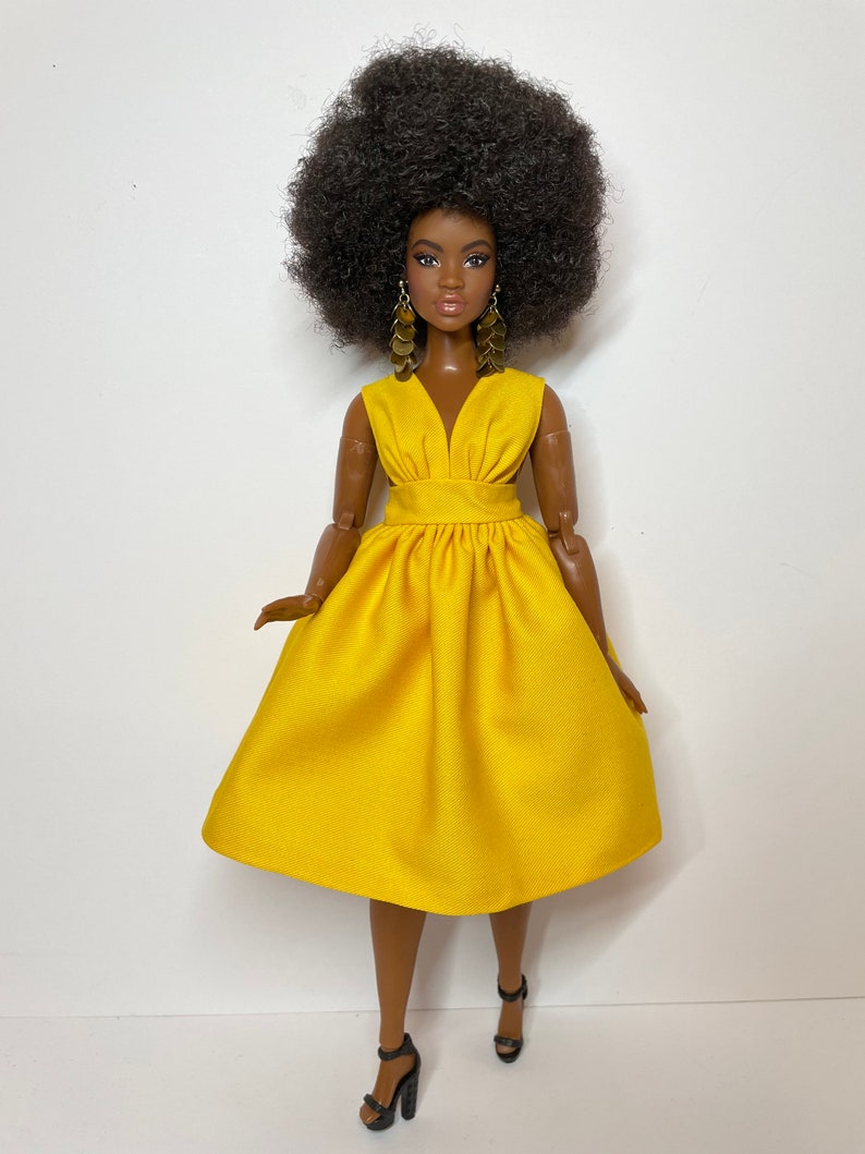 May include: A black doll with an afro hairstyle wearing a yellow dress and black heels.