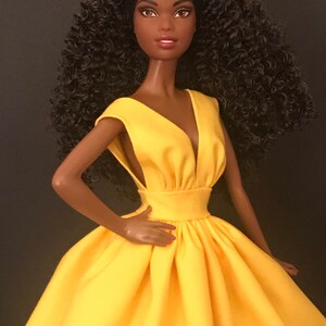May include: A black doll with curly brown hair wearing a yellow sleeveless dress with a V-neckline.