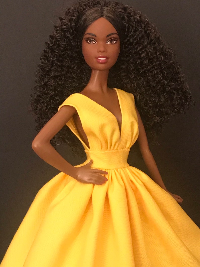 May include: A black doll with curly brown hair wearing a yellow sleeveless dress with a V-neckline.
