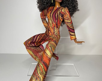 May include: A fashion doll with long, curly black hair wearing a red, orange, and gold patterned jumpsuit and red heels.