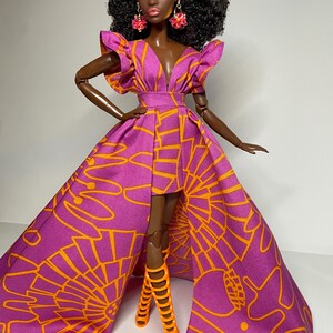May include: A fashion doll wearing a purple and orange dress with a high slit and matching orange high-heeled boots. The doll has dark skin, black curly hair, and pink earrings.