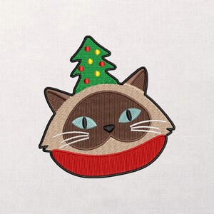 May include: Embroidered cat face with a Christmas tree hat and a red scarf. The cat has brown fur, blue eyes, and white whiskers. The Christmas tree is green with red and yellow ornaments.