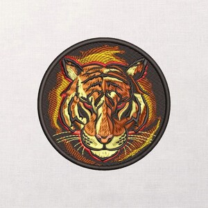 May include: Embroidered patch featuring a tiger's head with orange and black stripes, red eyes, and a pink nose. The tiger is set against a fiery orange and yellow background, all within a black circular border. The patch is likely for clothing or accessories.