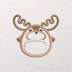 Puede incluir: Diseño bordado de una cabeza de alce de dibujos animados. El alce tiene grandes astas curvas, un contorno marrón y una boca ovalada blanca. Los ojos y la nariz son negros. El diseño está sobre un fondo blanco.