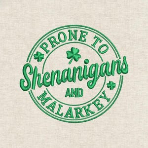 以下が含まれることがあります： ベージュの背景に緑色の刺繍で「PRONE TO Shenanigans AND MALARKEY」と書かれたデザイン。円形に配置され、シャムロックのアクセントが施されています。聖パトリックの日に適しています。