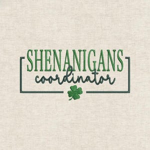 May include: Embroidered design on a beige fabric. The text reads "SHENANIGANS coordinator" in green and dark teal script, enclosed in a dark teal rectangle. A green four-leaf clover is below the text. The design has a textured appearance.