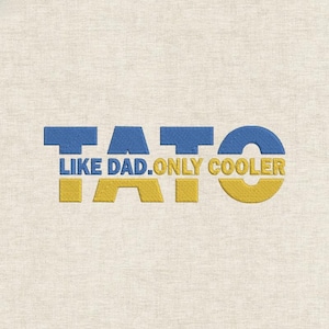 May include: Embroidered text on a beige fabric reads "TATO LIKE DAD. ONLY COOLER" in blue and yellow. The text is stylized with a bold, blocky font, creating a visually striking design. The fabric has a subtle, textured appearance.