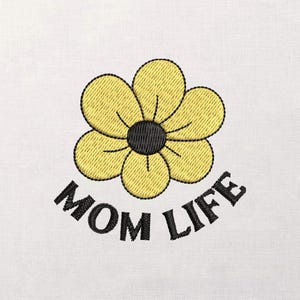 Peut inclure: Motif brodé d'une fleur jaune avec un centre et un contour noirs. Les mots "MOM LIFE" sont arqués en dessous de la fleur en noir. Le motif est sur un fond de tissu blanc.