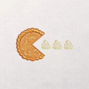 May include: Embroidered design featuring a pie slice with a Pac-Man-like shape, and three cream-colored, swirl-shaped objects. The pie is light brown with a textured appearance and a scalloped edge. The background is white.