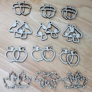 Könnte beinhalten: Ein Set mit 18 unfertigen Holzohrringen in verschiedenen Herbstformen, darunter Eicheln, Pilze, Äpfel und Ahornblätter. Die Ohrringe sind bereit zum Bemalen oder Beizen.