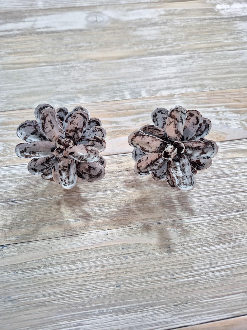 May include: Two decorative pine cone shaped objects with a white and gray marbled design. The objects are on a light wood surface.