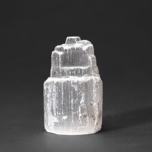 Op de afbeelding: Een wit selenietkristal met een gelaagde, gestapelde vorm. Het kristal is glad en doorschijnend, met een licht troebele uitstraling.