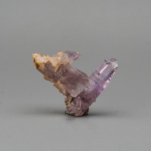May include: A cluster of amethyst crystals with a purple hue and clear quartz points. The crystals are arranged in a cluster, with the largest crystal in the center.