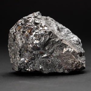 Può includere: Un grande masso metallico grigio scuro con una superficie ruvida e testurizzata. La roccia ha una struttura cristallina con molte piccole sfaccettature lucide.